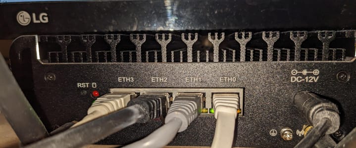 Front of the black fanless router with four Ethernet ports, ETH0 to ETH3, all plugged in, and a 12 V power jack